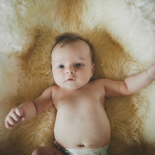 Cute, naked baby girl lying on sheepskin blanket in basket